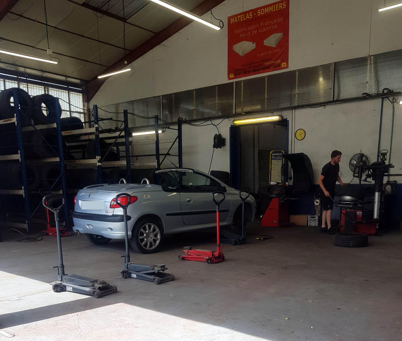 Un mécanicien au travail dans l'atelier, pneus d'occasion empilés sur le sol